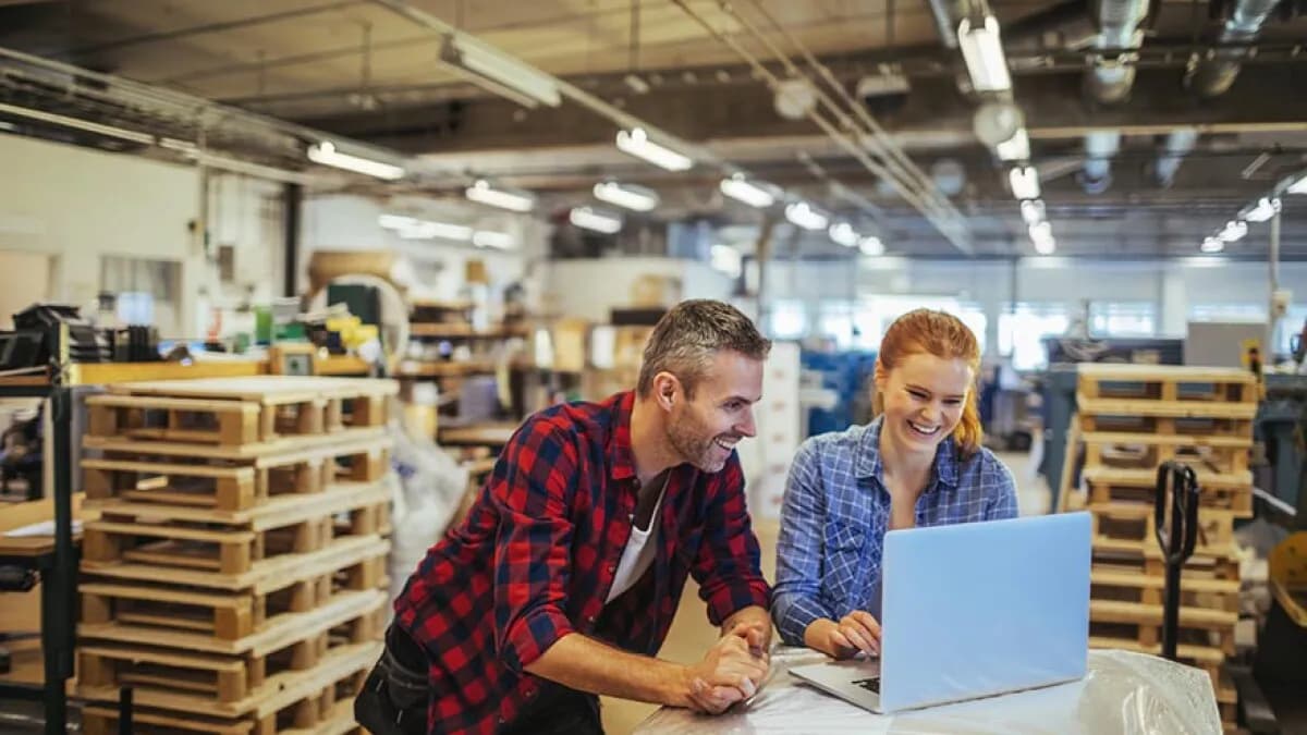 Two people in a warehouse looking at an open laptop and smiling