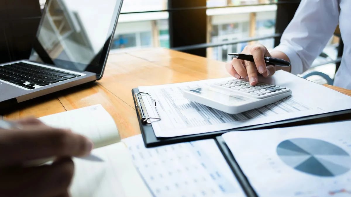 Two people sitting at a desk with papers and a calculator