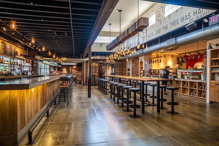 Interior of Wood Stack Pizza Kitchen restaurant with wood floors, tall tables with stools and a bar