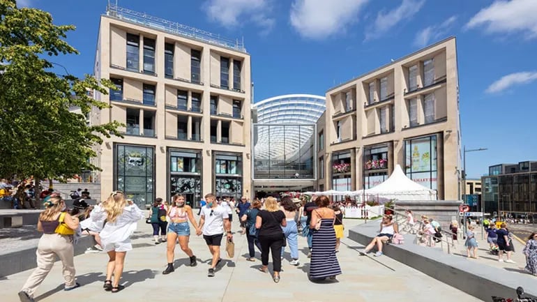 Crowds of people walking outside with a four story shopping center building in the background