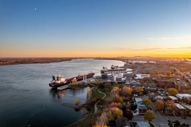 Oil tankers unloading in their cargo in the Port of Montreal. In the fore ground we see the Saint-Lawrence River and in the background we see the Montreal skyline at a distance.