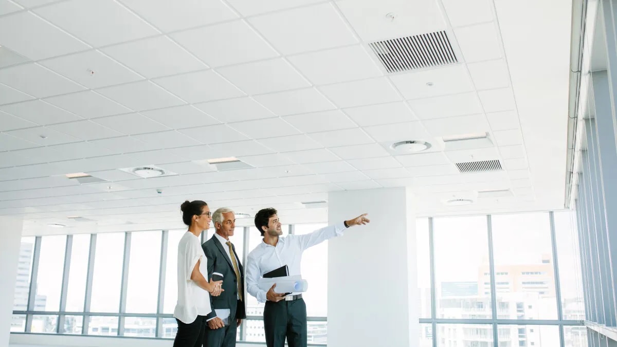 Three people in an empty white room with one person pointing at the wall