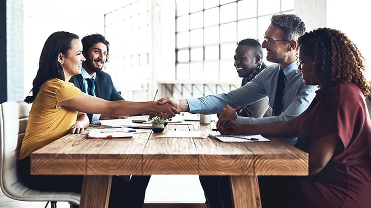 Five people sitting at a table with two people shaking hands