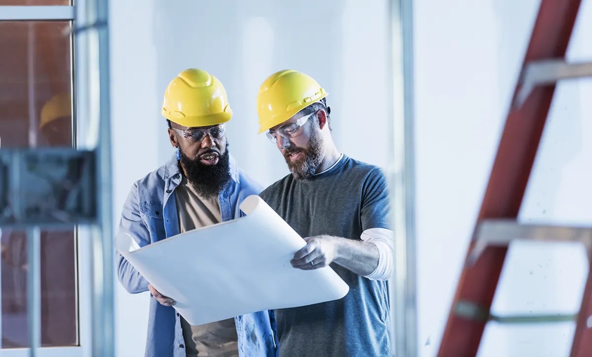 Two construction workers standing in hard hats looking at plans