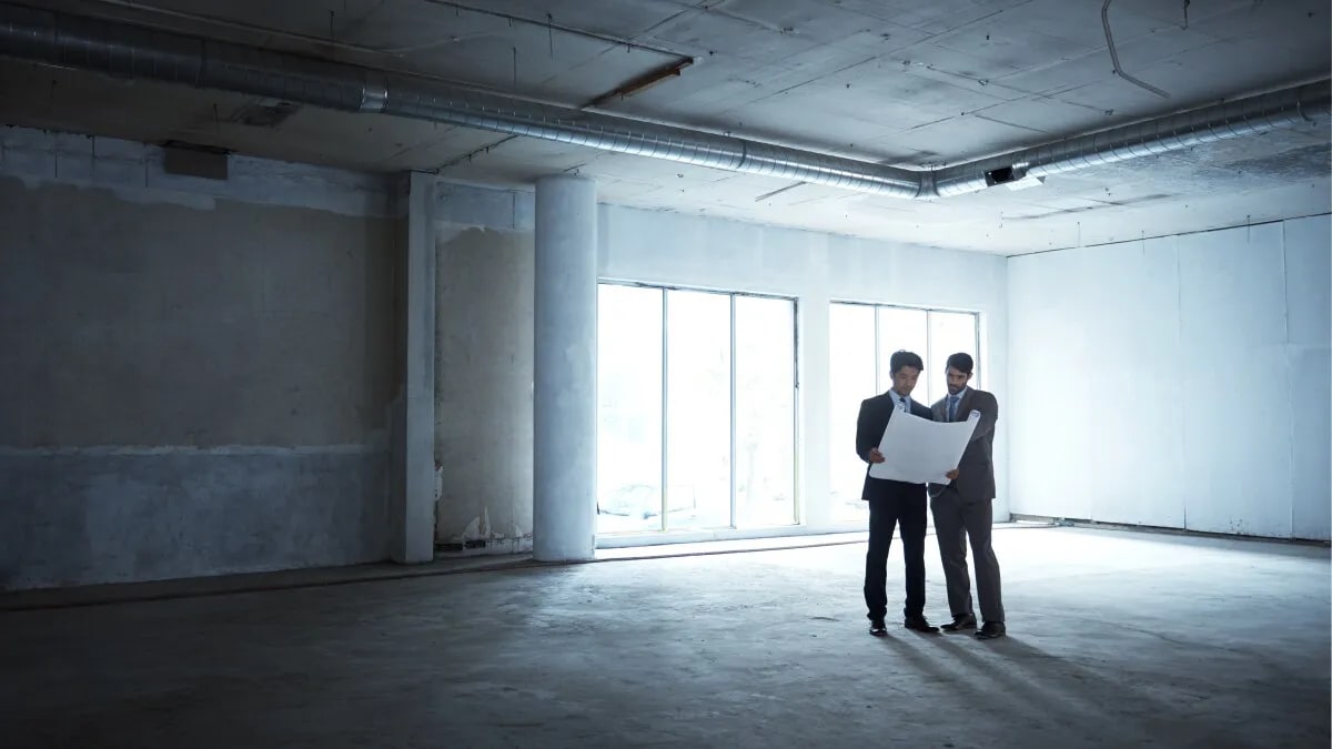 Two people standing in an empty office space looking at plans