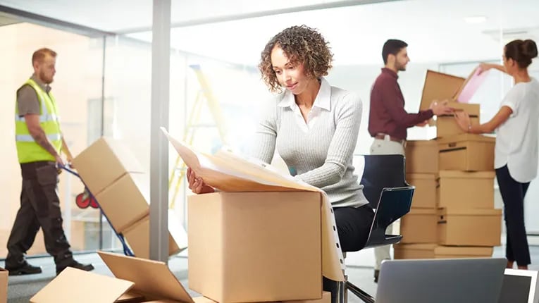 A woman looking through a box with people behind her moving boxes