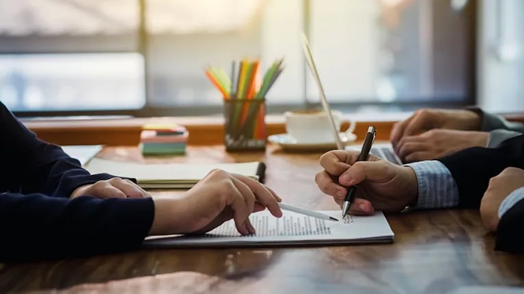 a desk showing the hands of two people signing paperwork